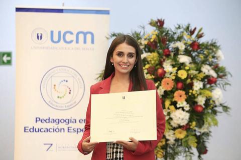 Una joven sonriente sostiene un certificado frente a un fondo decorativo de flores y un cartel de la universidad.