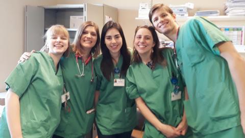 Cinco profesionales de la salud sonríen juntos en un entorno médico.