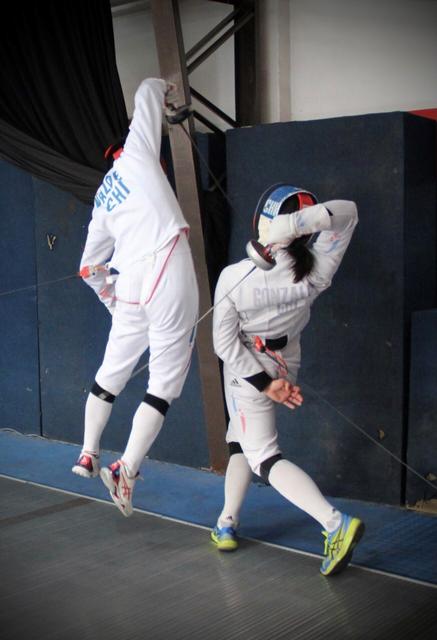 Dos esgrimistas en plena competencia, uno realizando un salto mientras el otro defiende con la espada.