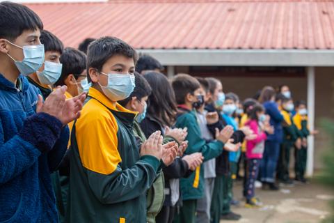 Un grupo de niños aplaudiendo al aire libre, todos portando mascarillas.