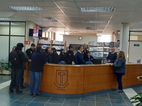 Un grupo de personas en un área de recepción de una universidad, conversando y esperando atención.