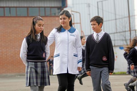Tres estudiantes interactúan en un patio escolar.