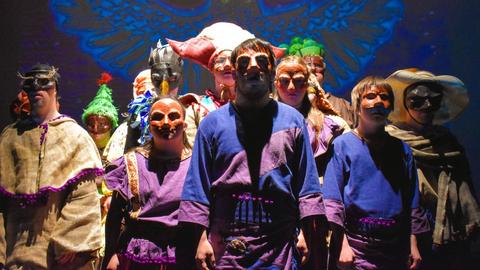 Un grupo de personas con máscaras y vestimenta tradicional en una presentación teatral.