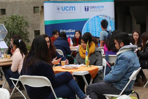 Un grupo de personas socializando en una mesa durante un evento universitario al aire libre.