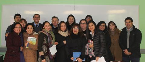 Un grupo de personas sonrientes posando juntas en un aula con una pizarra blanca al fondo.