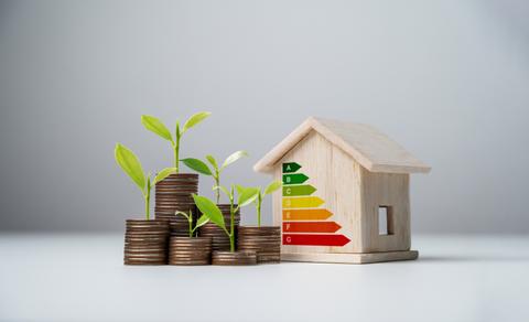 Una casa de madera junto a monedas y plantitas que representan el ahorro y la sostenibilidad.