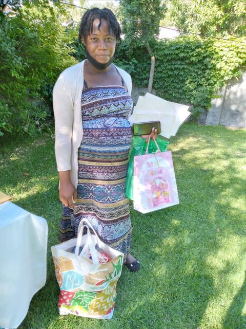 Una mujer sostiene varias bolsas mientras sonríe en un entorno al aire libre con césped verde.