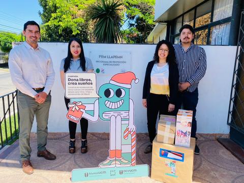 Un grupo de cuatro personas posando frente a un cartel que promueve una campaña de donación de libros.