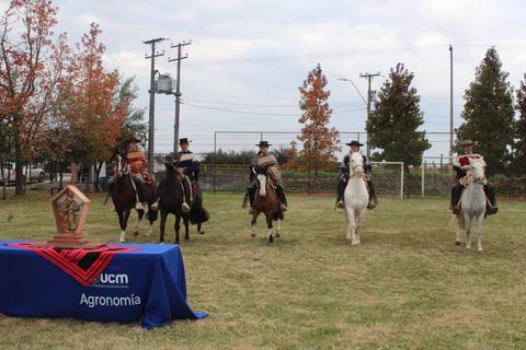 Un grupo de jinetes a caballo se desplaza frente a una mesa con un mantel que dice Agronomía.