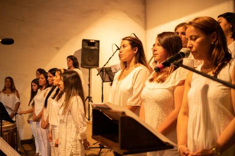 Un grupo de mujeres vestidas de blanco cantan en un escenario.