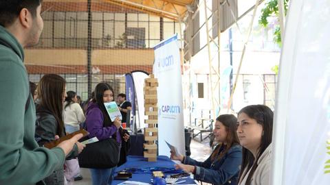 Una feria educativa donde estudiantes interactúan en un stand con información de carreras.