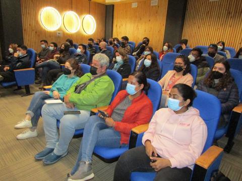 Un grupo de personas con mascarillas sentadas en un auditorio durante una presentación.