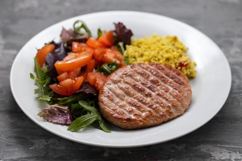 Un plato que incluye una hamburguesa de carne, ensalada mixta y couscous.