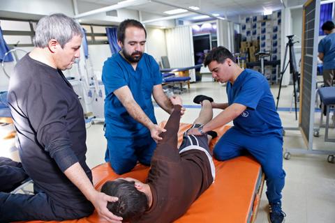 Un grupo de terapeutas físicos están ayudando a un paciente en una sesión de rehabilitación.
