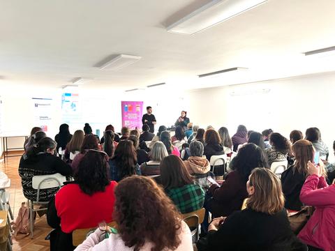 Un grupo grande de personas asistiendo a una charla en un salón iluminado.