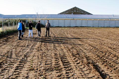 Un grupo de personas observa un terreno arado frente a una construcción.