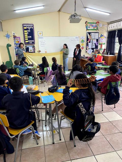 Un aula de clases con estudiantes atentos mientras un grupo presenta un trabajo.