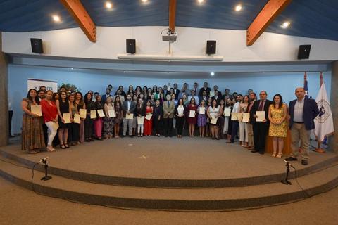 Un grupo grande de personas posando en un escenario, sosteniendo certificados de reconocimiento.