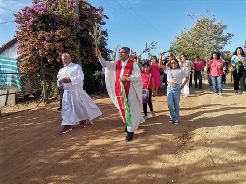 Una procesión con un sacerdote y un grupo de personas caminando por un camino de tierra.