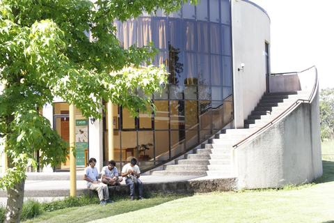 Tres personas sentadas en un banco frente a un edificio moderno con grandes ventanales.