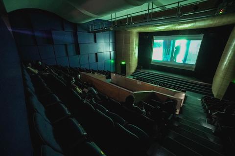 Una sala de cine con asientos vacíos y una pantalla proyectando una película en un ambiente oscuro.