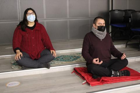 Dos personas meditando en un ambiente interior con elementos de confort.