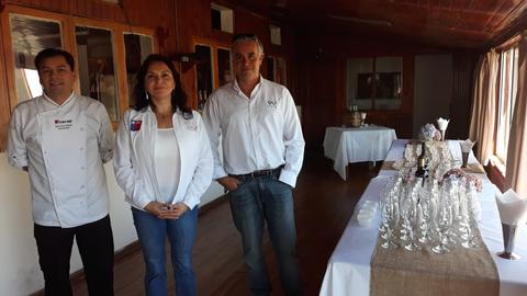 Tres personas posan frente a una mesa decorada con copas y utensilios en un ambiente cálido.