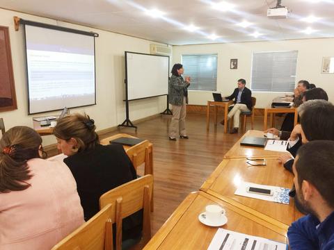 Una reunión en un salón donde se presenta información en una pantalla mientras varias personas escuchan.