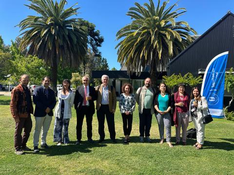 Un grupo de personas posando en un jardín con palmeras y un edificio al fondo.