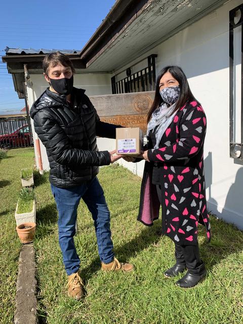 Una pareja de personas intercambiando un objeto en un entorno exterior frente a una pared blanca.