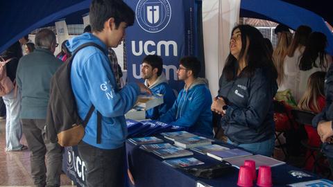 Un grupo de personas en un stand informativo con material promocional de una universidad.