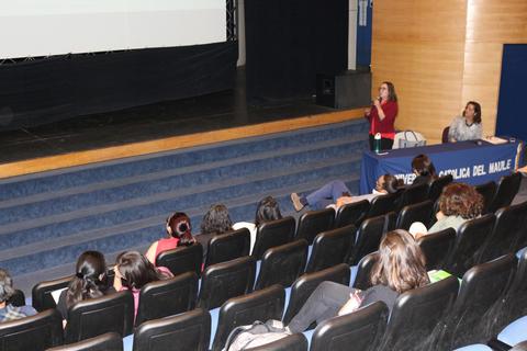 Una presentadora habla frente a un público en un auditorio durante una conferencia.
