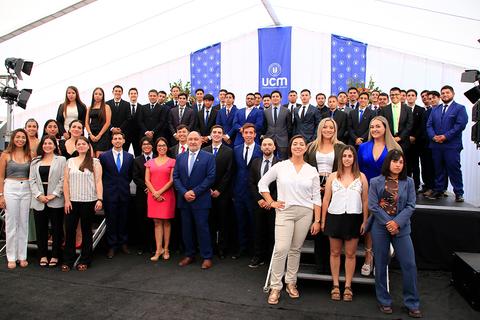Un grupo de personas en un evento formal, posando en un escenario con un fondo decorado.