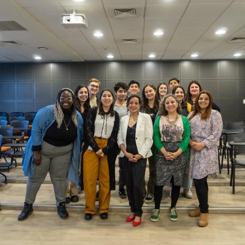 Un grupo diverso de personas sonríe para la foto en un ambiente interior con asientos en el fondo.