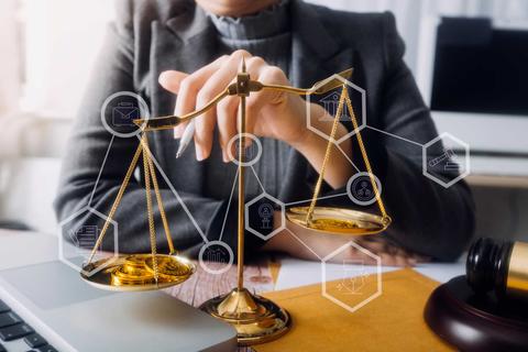 Una persona sostiene una balanza de la justicia sobre una mesa de trabajo, acompañada de símbolos legales.