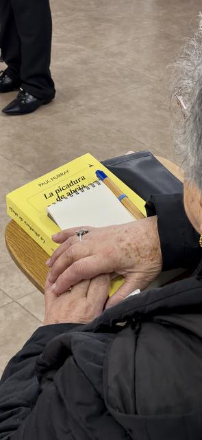 Una señora mayor sostiene un libro titulado 'La picadura de la alacrana' sobre una mesa.