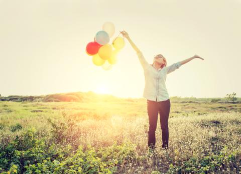 Una persona alegre sostiene globos en un campo mientras disfruta de un atardecer.