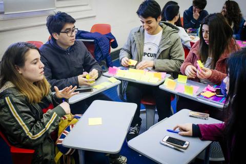Un grupo de estudiantes en una sala de clase compartiendo ideas con post-it.