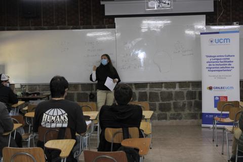 Una profesora da una clase en un aula con estudiantes atentos.