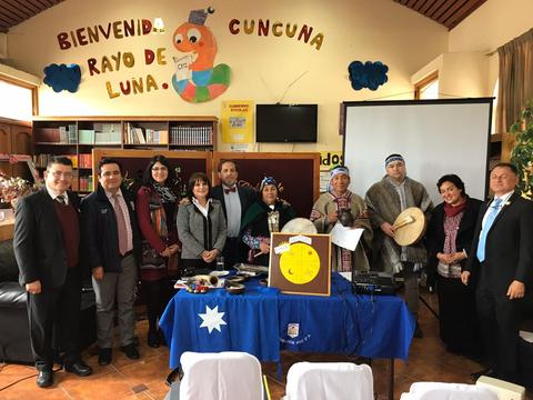 Grupo de personas posando frente a una mesa en un evento cultural en una biblioteca.