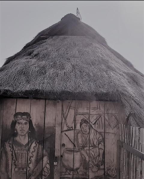 Una casa con techo de paja y murales en la puerta que representan a personas en actividades cotidianas.