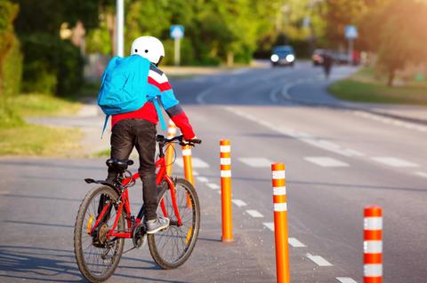 Un cabro chico pedaleando por la calle con casco y mochila.