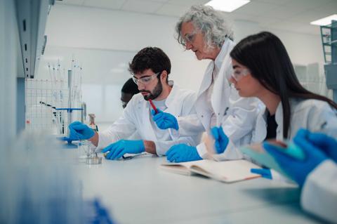 Un grupo de estudiantes y una profesora trabajan juntos en un laboratorio.