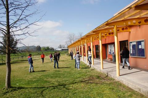 Un grupo de personas se encuentra en el exterior de un edificio escolar rodeado de un paisaje verde.