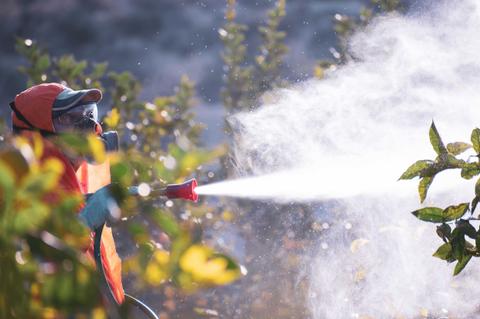 Un trabajador rocía plantas con un equipo de protección y un dispositivo pulverizador.