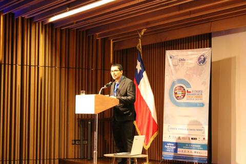 Un hombre está hablando desde un podio en un evento en Chile, con una bandera chilena de fondo.