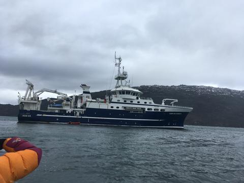 Un barco de investigación se encuentra en el agua con montañas al fondo.