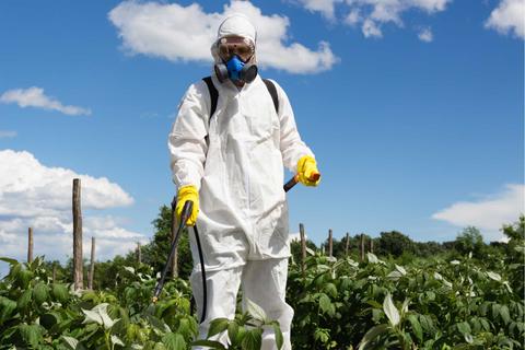 Un trabajador agrícola vestido con equipo de protección personal está aplicando pesticidas en un campo.