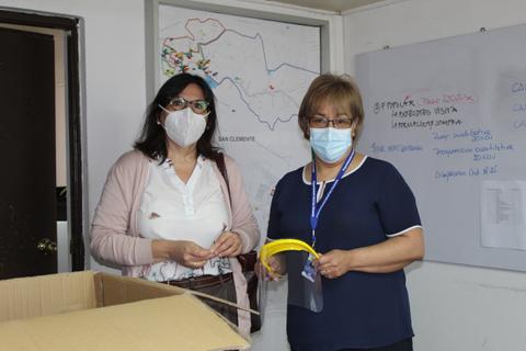 Dos mujeres, usando mascarillas, sostienen elementos de protección personal en una oficina.