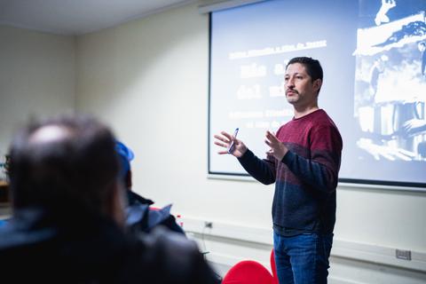 Un profesor está dando una charla en un salón de clases con una presentación detrás.